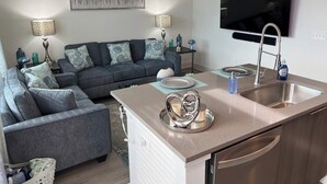 A modern living room with a grey sofa, a small kitchen area with a sink and a flat-screen TV mounted above it. - Cozy 1-Bedroom Studio in Tranquil Atlanta (Atlanta)