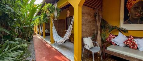 A yellow building with a hammock, a bench, and a painting.