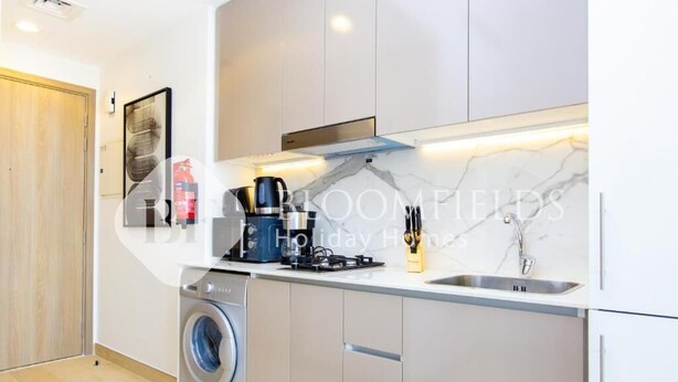 A modern kitchen with a built-in washing machine, a coffee maker, and a sink. - Bloomfields Stu Riviera Skies (Dubai)