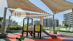 An outdoor play area with a climbing structure, slide, and colorful ground cover. - Bloomfields Stu Riviera Skies (Dubai)
