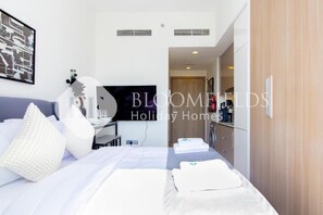 Camera d'albergo con un letto, cuscini, una scrivania, un televisore e un bagno parzialmente visibile da una porta aperta.