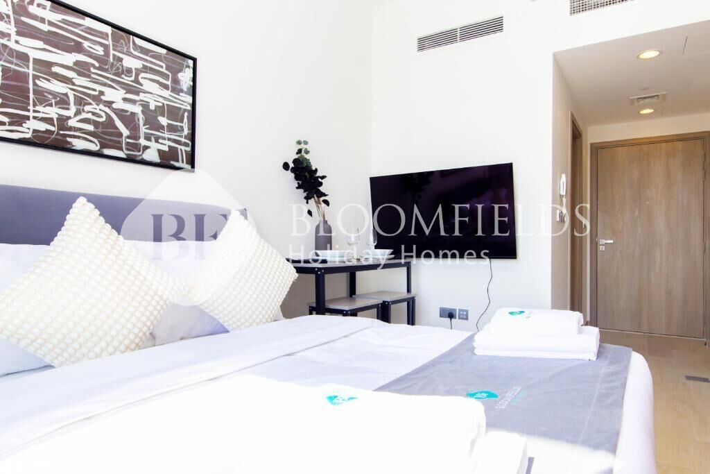 Una habitación de hotel con cama, almohadas, televisor, escritorio y puerta.