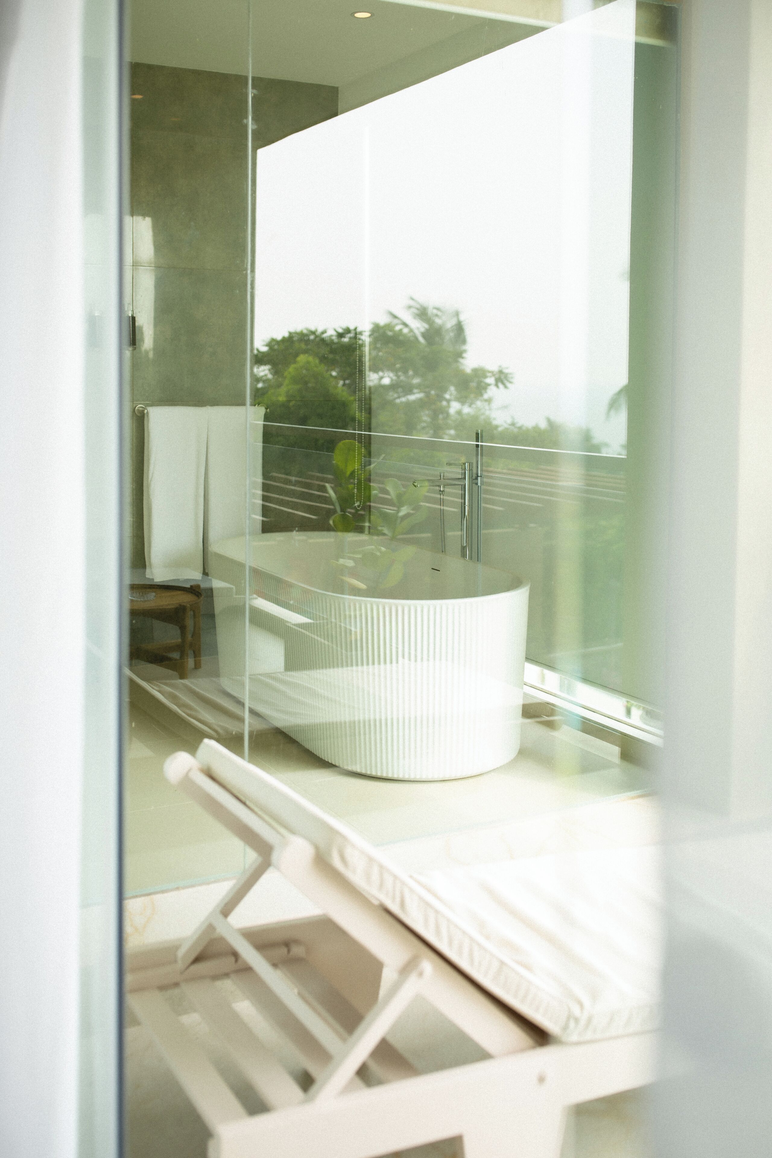 A modern bathroom with a glass-enclosed bathtub, a white sink, and a white chair.