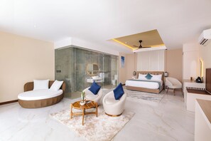 Een moderne hotelkamer met een rond zithoekje, een bed met hoofdeinde, een douchecabine met glazen wanden en een klein bureau met stoel.