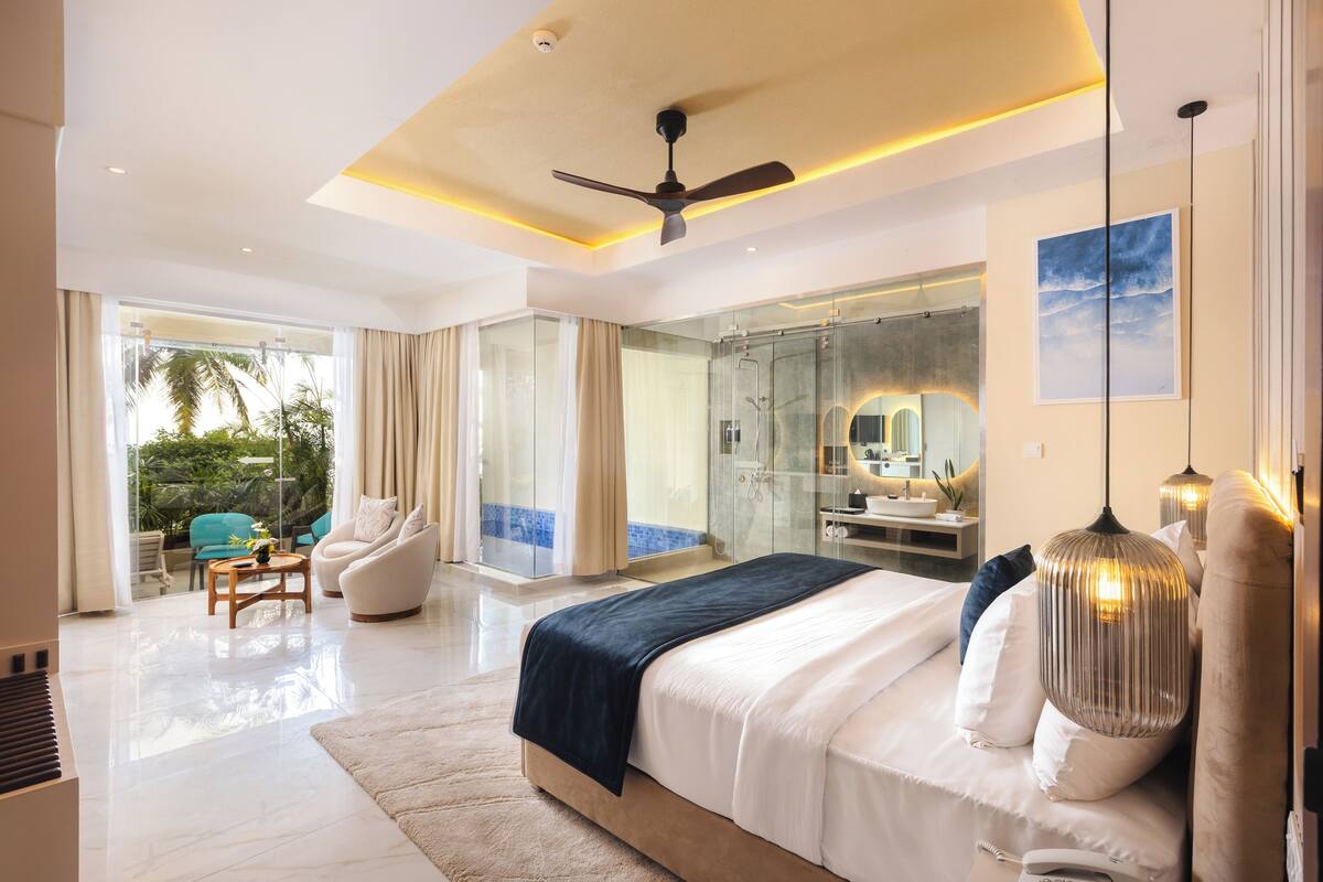 Ein modernes Schlafzimmer mit einem großen Bett, einem Deckenventilator, einer Glasdusche und Blick ins Freie.