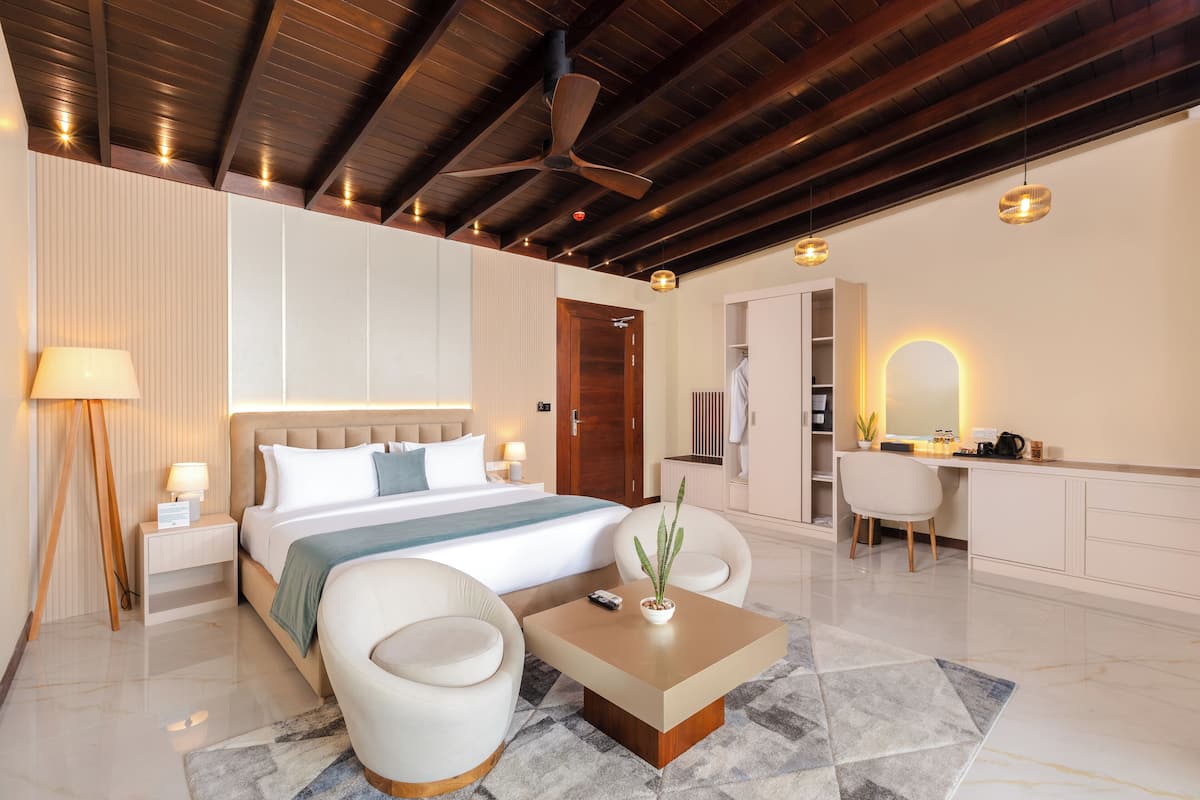 Ein Hotelzimmer mit Bett, Nachttischen, Schreibtisch, Stuhl, Couchtisch, Pflanze und einem Badezimmer mit Spiegel und Waschbecken.
