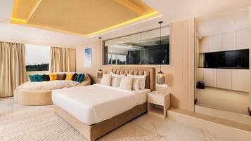 A modern bedroom with a large bed, a seating area, a TV, and a view of the outdoors.