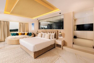 A modern bedroom with a large bed, a seating area, a TV, and a view of the outdoors.