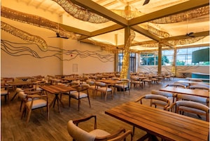 Un comedor espacioso con mesas y sillas de madera, un techo alto con lámparas de fibra y ventanas amplias que ofrecen vistas al exterior.