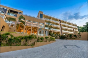 Un hotel de varios pisos con un diseño arquitectónico moderno, que cuenta con balcones, ventanas amplias y un patio ajardinado.