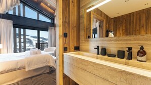 Une chambre d’hôtel moderne avec un grand lit, un mur décoratif en bois, une salle de bain dotée d’un grand miroir et une vue sur un paysage enneigé.