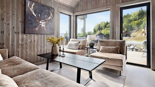 A modern living room with a large window, a mounted deer painting, and a cozy seating area. - New and Great Cabin at the Foot of Norefjell (Krodsherad)