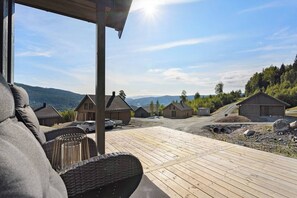 A wooden deck with wicker furniture, overlooking a residential area with houses and mountains. - New and Great Cabin at the Foot of Norefjell (Krodsherad)