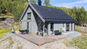 A modern cabin with a sloped roof, a deck with outdoor furniture, and a chimney. - New and Great Cabin at the Foot of Norefjell (Krodsherad)