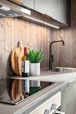 A modern kitchen with a stainless steel sink, wooden cutting board, wine bottle, and potted plant.