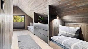 A loft bedroom with a sloped ceiling, built-in wooden wardrobe, a bed with a striped blanket, and a potted plant on the dresser. - New and Great Cabin at the Foot of Norefjell (Krodsherad)