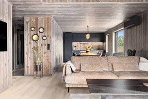 A modern living room with a sofa, a coffee table, and a dining area with a table and chairs. - New and Great Cabin at the Foot of Norefjell (Krodsherad)