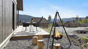 A wooden deck with outdoor furniture, a fire pit, and a view of surrounding houses and hills. - New and Great Cabin at the Foot of Norefjell (Krodsherad)