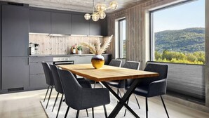 A modern kitchen with dark cabinets, a wooden dining table, and chairs. There is a large window with a view of a forested area. - New and Great Cabin at the Foot of Norefjell (Krodsherad)
