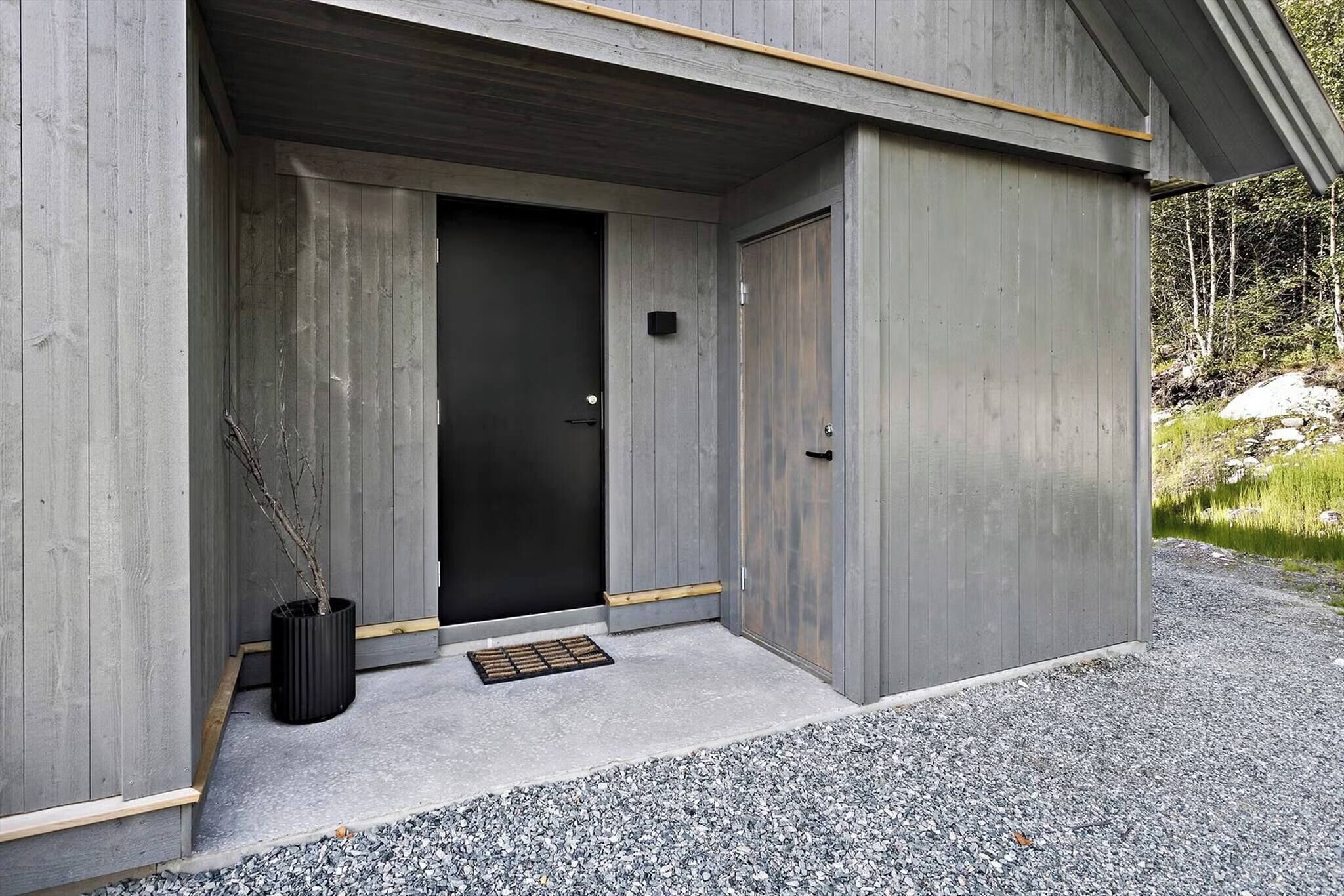 A modern building with a concrete exterior, a black door, and a small black planter with branches.