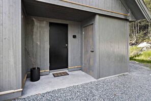 A modern building with a concrete exterior, a black door, and a small black planter with branches. - New and Great Cabin at the Foot of Norefjell (Krodsherad)