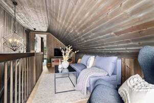 Un acogedor espacio tipo loft con techo de madera, un sofá azul, una mesa de centro y un televisor al fondo.