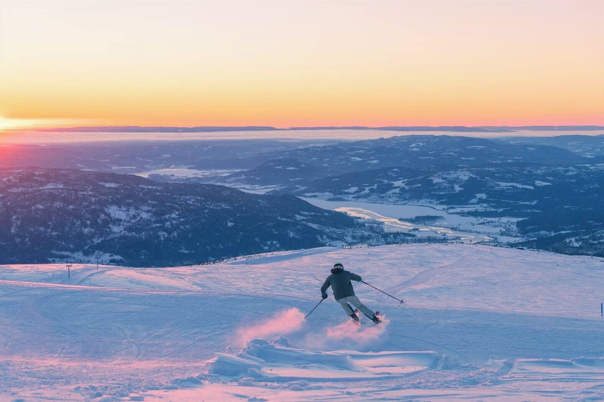 A skier on a snowy slope with a sunset in the background.