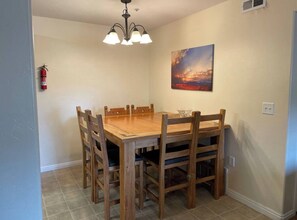 A dining room with a wooden table and chairs, a chandelier, a fire extinguisher, and a painting on the wall.