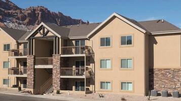 A multi-story hotel with balconies, stone accents, and a mountain backdrop.