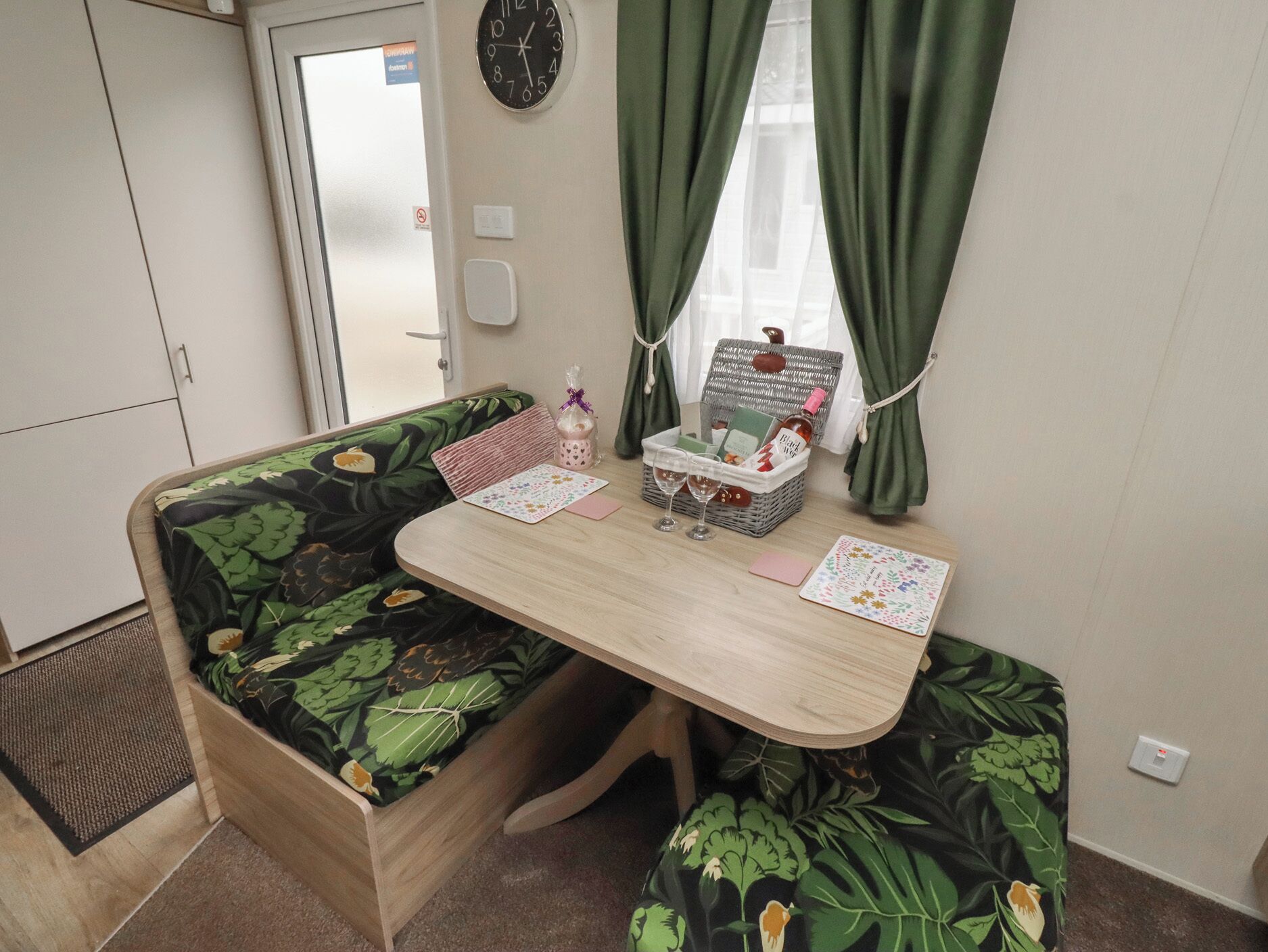 A compact living space with a sofa bed, a small table, a wicker basket with items, and a clock on the wall.