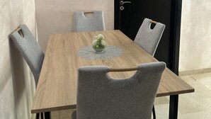 Une table à manger avec quatre chaises grises, une table en bois et un vase en verre contenant des fleurs, posé sur un chemin de table.