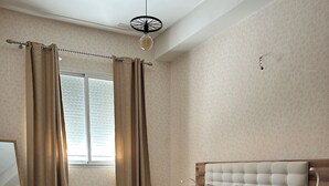 Une chambre à coucher avec un lit, une table de chevet, un miroir et une fenêtre avec des rideaux.