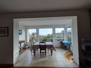 A dining area with a table and chairs, large windows with a view, and a television on the wall. - An exceptional spot! Apartment in a charming house, swimming at the bottom of the garden (Locmariaquer)