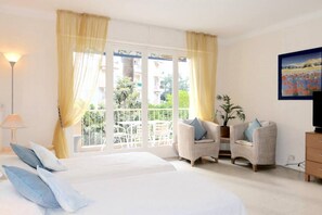 A hotel room with a bed, two armchairs, a TV, and a balcony with curtains. - Charming Cannes Studio with Private Balcony – Near Rue d’Antibes & Beaches (Cannes)