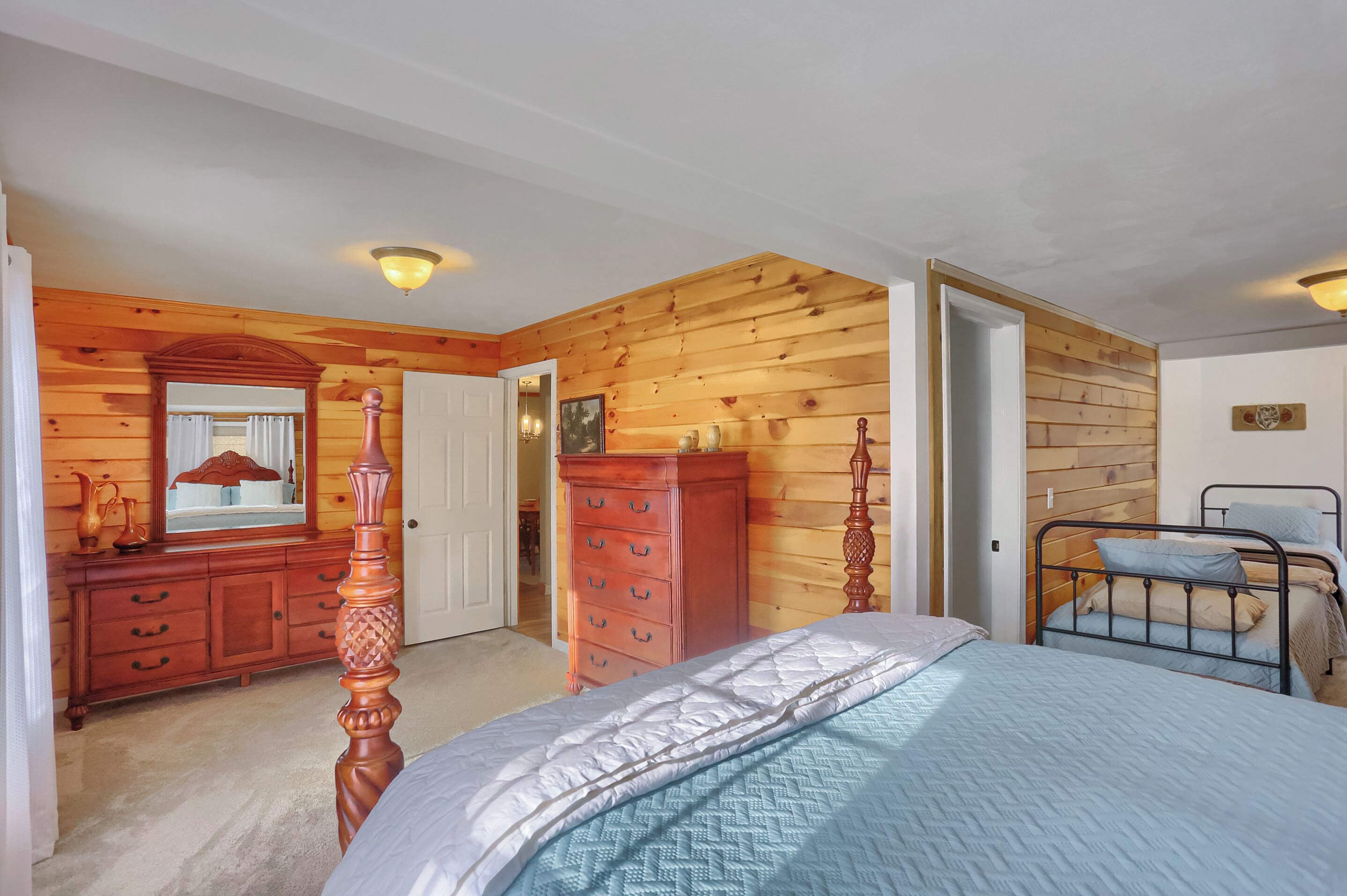Une chambre avec des lambris en bois, un lit, une commode et une table de chevet.