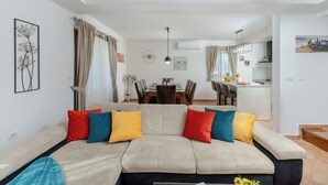 A modern living room with a beige sofa, colorful cushions, a dining area with a table and chairs, and a kitchen in the background. - Modern Villa in Istria with Heated Pool, Jacuzzi & Total Privacy (Nedešćina)