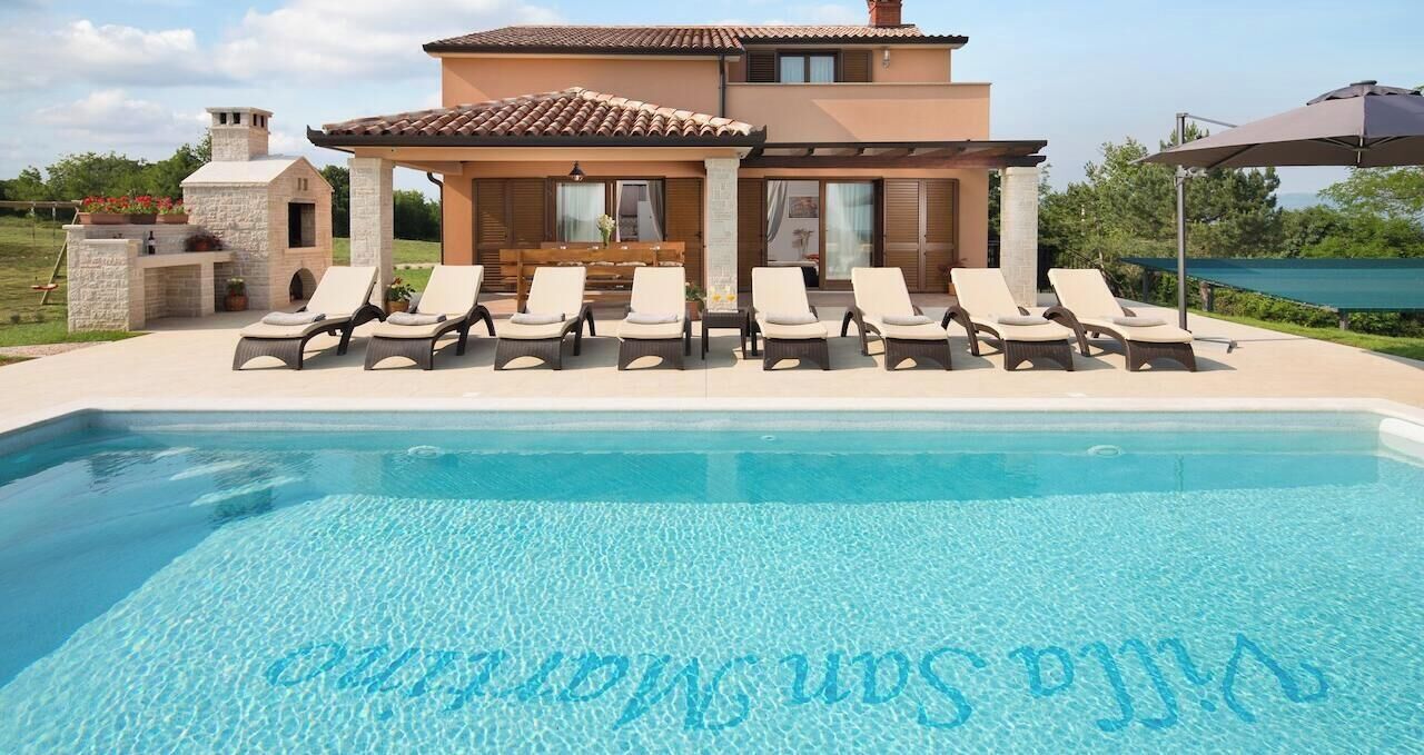 Zona de piscina con sillones de descanso y un edificio de piedra al fondo.