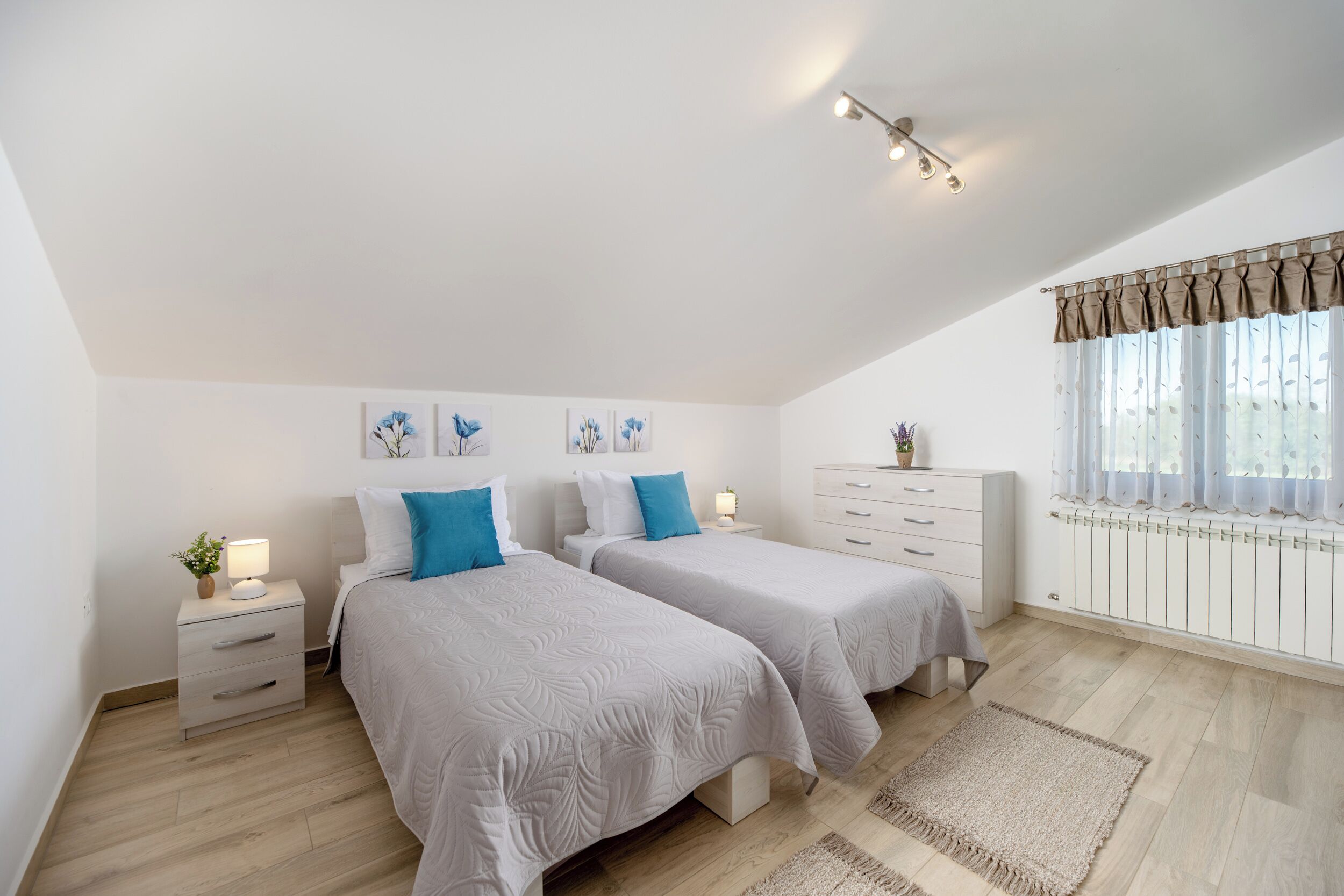 Une chambre avec deux lits, une table de chevet avec une lampe, une commode et une fenêtre avec des rideaux.