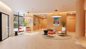 A modern hotel lobby with a herringbone floor pattern, a reception desk, seating area with chairs, and artwork on the walls.
