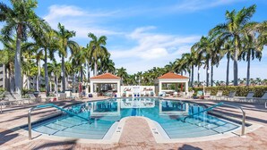 Piscina com espreguiçadeiras e palmeiras, ladeada por um caminho de tijolos.