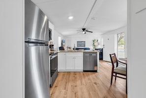 A modern kitchen with stainless steel appliances, wooden flooring, and a ceiling fan. - Seabreeze Serenity-2 Kings, 1 Queen, garage, large yard (Murrells Inlet)