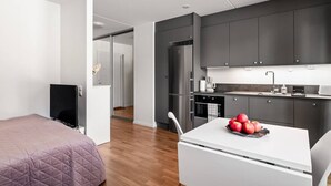 Una habitación de hotel moderna con cama, una mesita con manzanas, una kitchenette y un televisor.