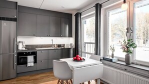 Una cocina moderna con gabinetes grises, una encimera blanca y una zona de comedor con mesa y sillas blancas.