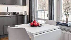 Una cocina moderna con armarios oscuros, una mesa de comedor blanca y vistas a árboles a través de amplios ventanales.
