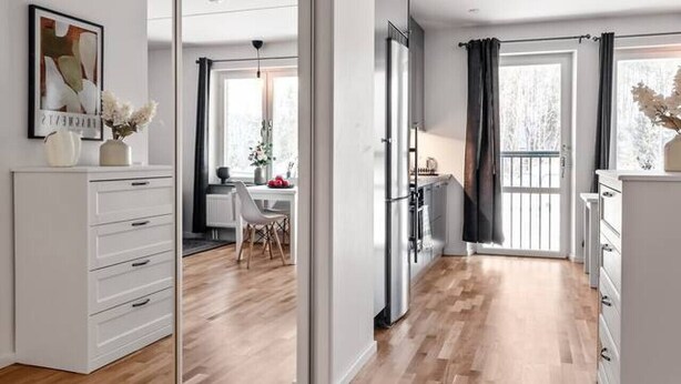 Un interior moderno con piso de madera, armarios blancos, un comedor y una cocina con refrigerador.