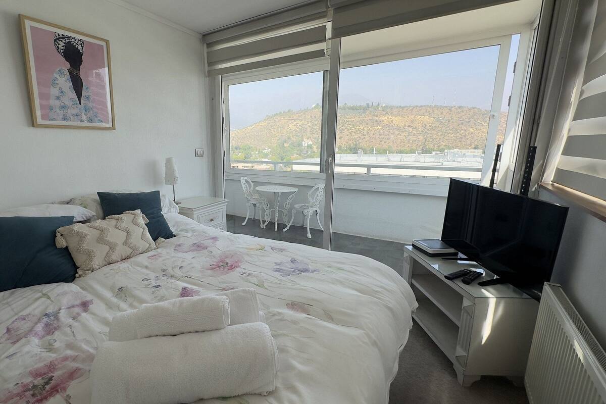 Ein Hotelzimmer mit Bett, Fernseher, Schreibtisch mit Laptop, Stuhl und einem Balkon mit Blick.