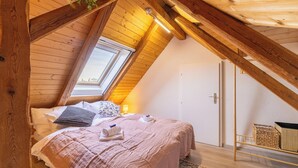 Une chambre mansardée chaleureuse, avec un plafond en pente, un puits de lumière, un lit recouvert d'une couverture rose et un panier en osier.
