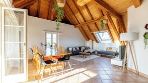 Un loft spacieux avec un haut plafond en bois, un coin repas comprenant des chaises et une table, un canapé et un téléviseur.