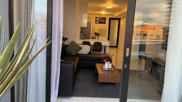 A modern living room with a sofa, a coffee table, and a dining area. - 77 on Independence Apartments (Windhoek)