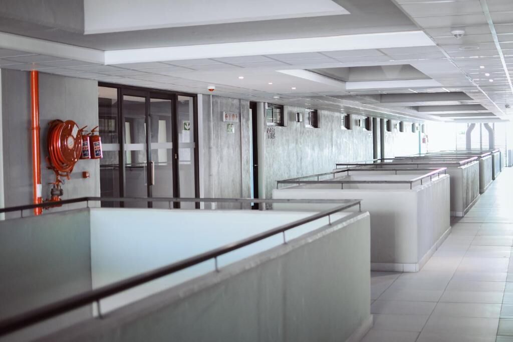 Un pasillo moderno de hotel con barandillas de vidrio, extintores y un piso limpio de baldosas.
